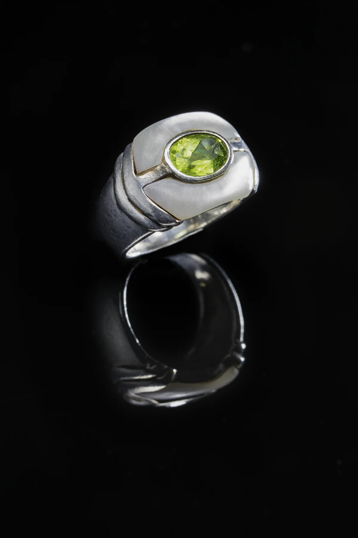 Bague Spinelle à pierre verte claire et entourage lumineux sur fond noir